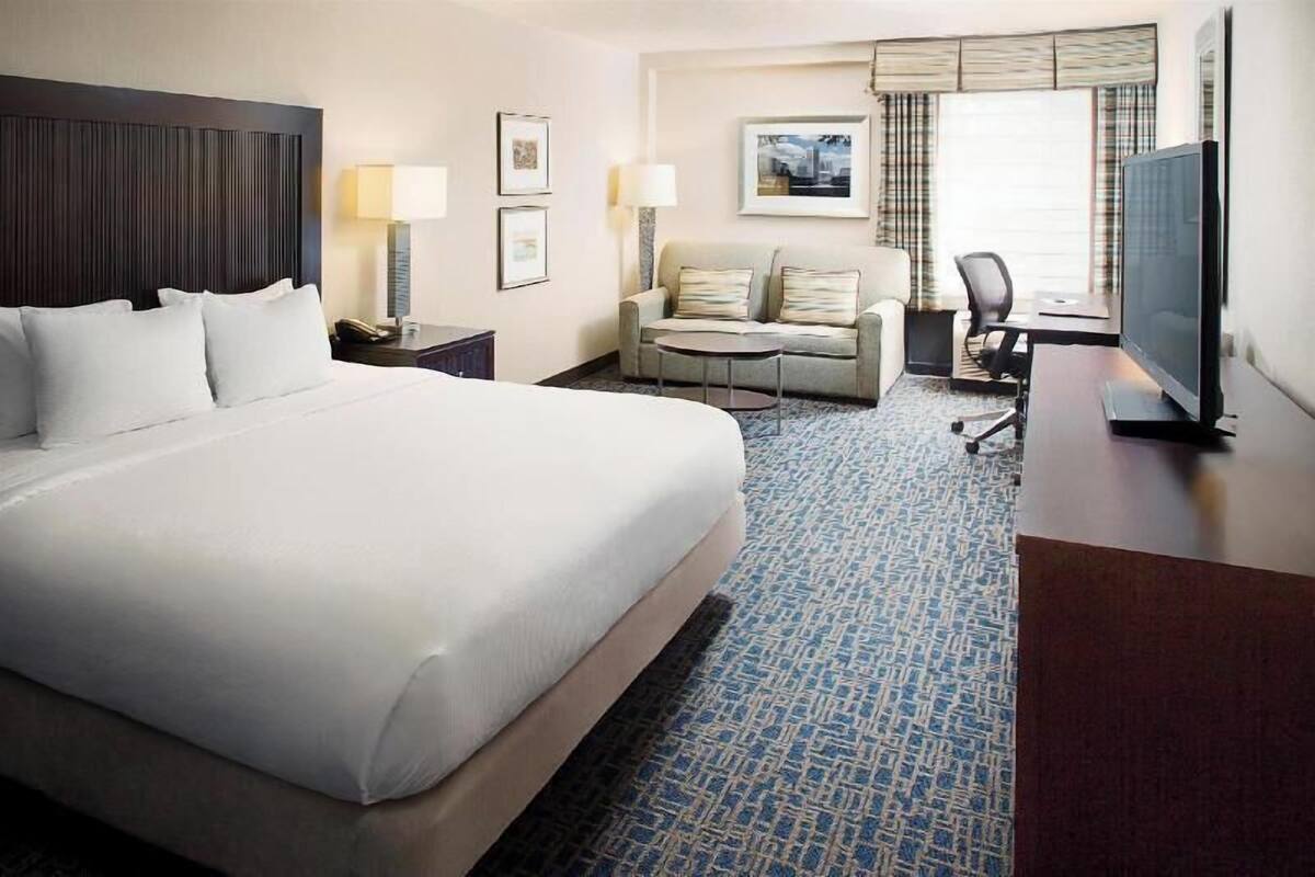 A hotel room with a large bed, a sofa, a desk with a TV, and a window with curtains.