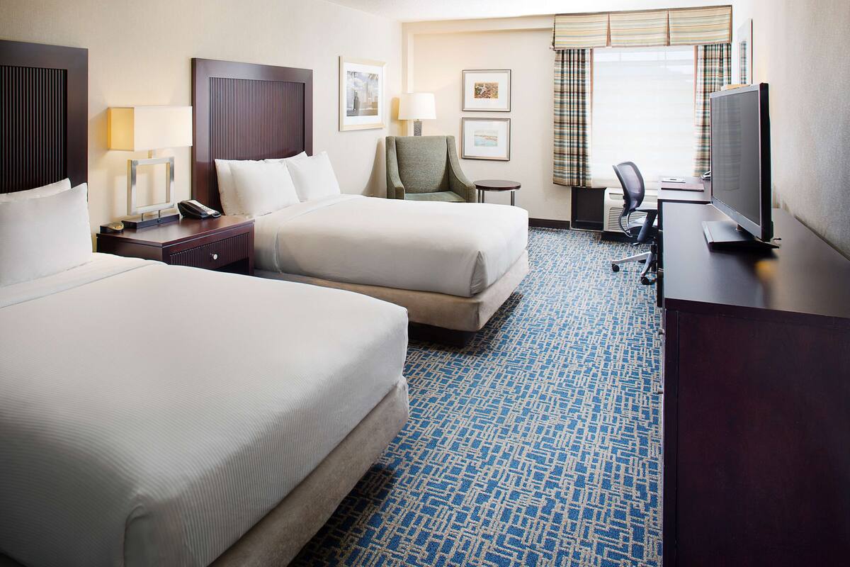 A hotel room with two beds, a desk with a computer, a TV, and a chair.