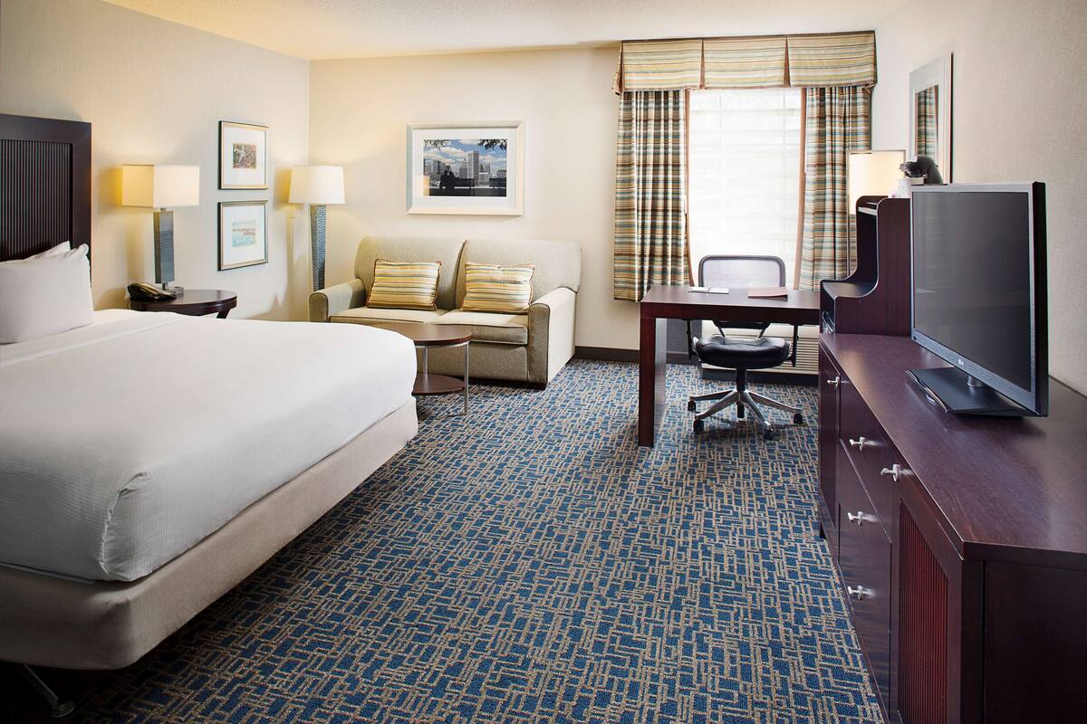 A hotel room with a large bed, a desk with a chair, a television, and a sofa.