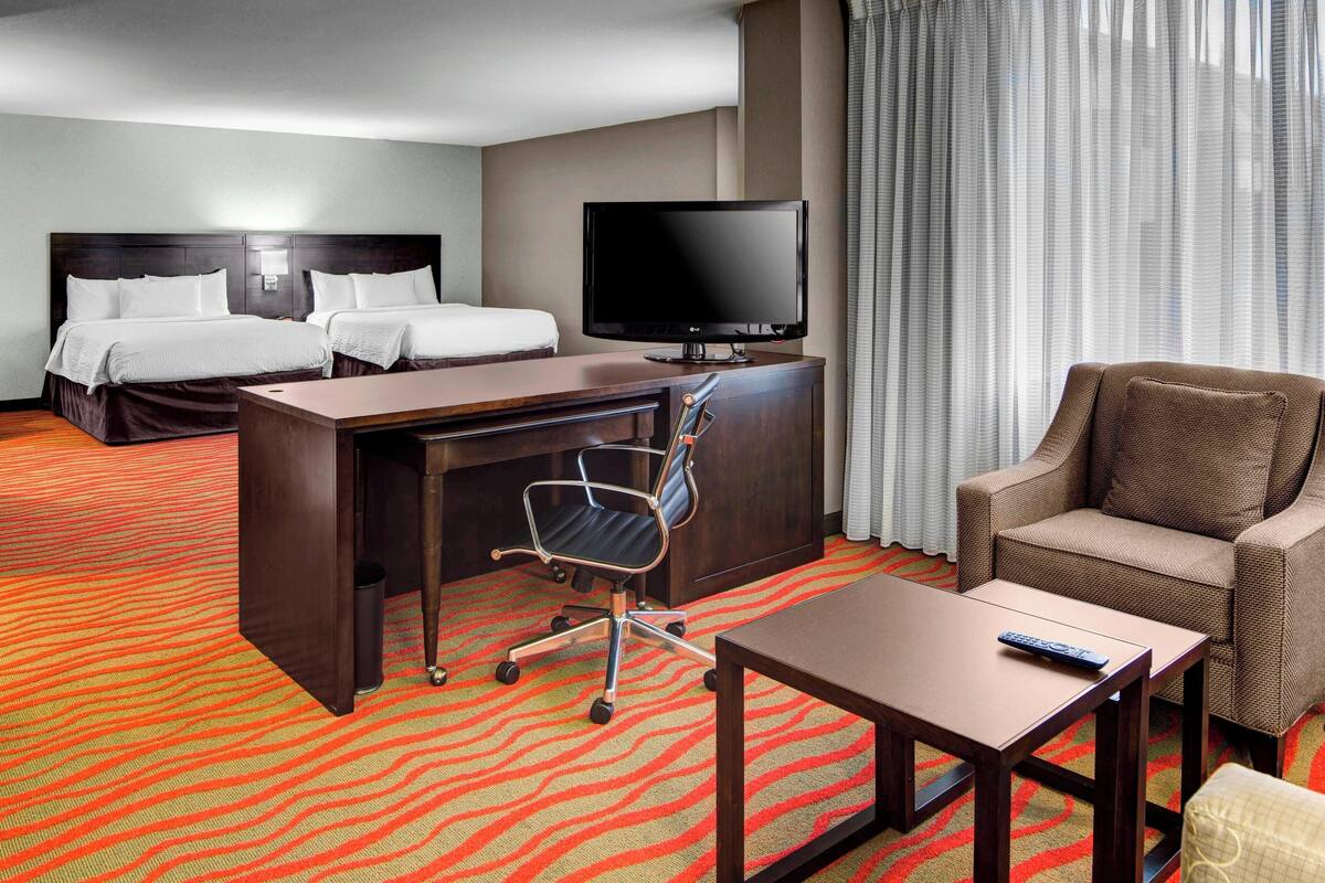 A hotel room with two beds, a desk with a chair, a television, and a sofa.