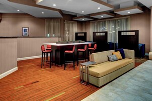Habitación de hotel con piso de madera, un sofá, una pequeña mesa y una zona de bar con taburetes.