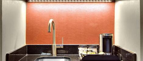 Una cocina compacta con microondas, cafetera y lavamanos.