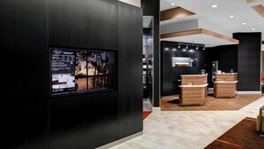 A modern hotel lobby with a digital display, reception area, and wooden reception desks. - Courtyard St. Cloud (St Cloud)
