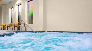 A hot tub with a metal ladder, surrounded by chairs and a tiled floor, with windows and a brick wall in the background. - Courtyard St. Cloud (St Cloud)