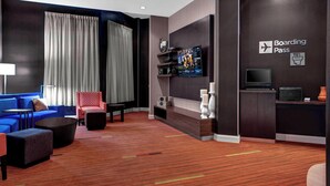 A modern hotel lobby with a blue sofa, a red armchair, a flat-screen TV, and a 'Boarding Pass' sign. - Courtyard St. Cloud (St Cloud)