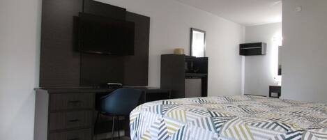 A hotel room with a bed, a desk, a chair, a TV, and a mirror.