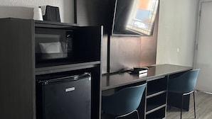 A compact hotel room with a kitchenette, a flat-screen TV mounted on the wall, and two chairs. - Motel 6 Brookhaven, MS (Brookhaven)