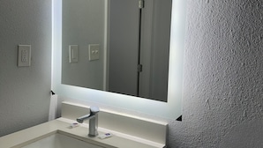 A bathroom with a white sink, a mirror, and a light fixture above the mirror. - Motel 6 Brookhaven, MS (Brookhaven)