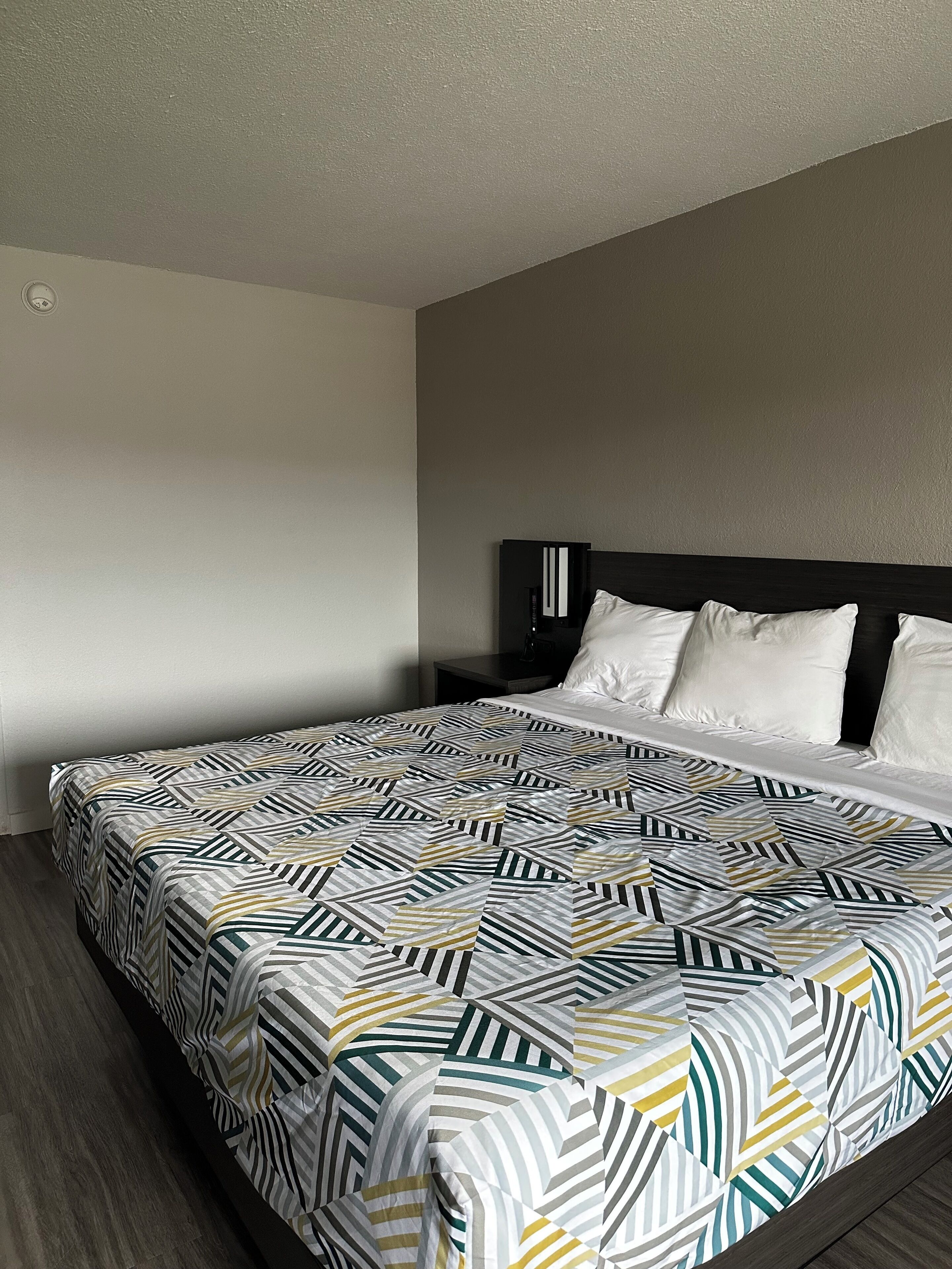 Una habitación de hotel con una cama grande, un cabecero oscuro y una pared lisa.