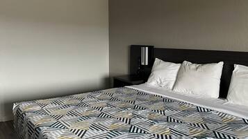 A hotel room with a large bed, a dark headboard, and a plain wall.