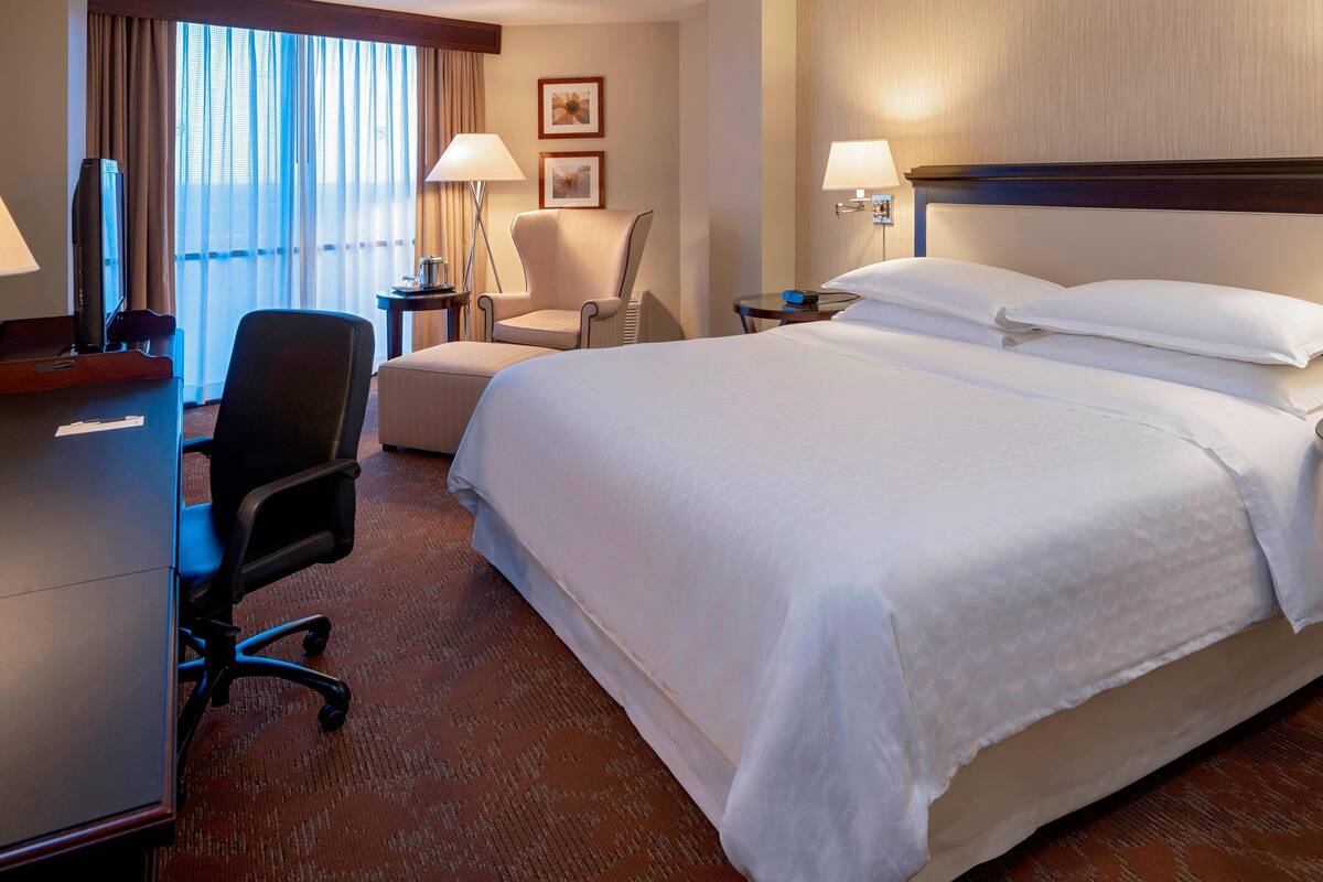 A hotel room with a large bed, a desk with a computer, a chair, and a TV.
