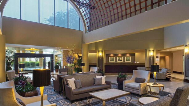 A spacious lobby with a high ceiling, comfortable seating areas, and a view of the outdoors.