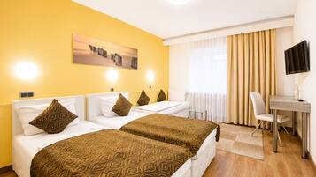 A hotel room with two beds, a desk, a chair, a TV, and a window with curtains.