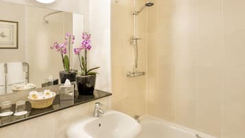 A bathroom with a sink, mirror, shower, and potted orchids.