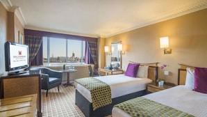 A hotel room with two beds, a desk, a chair, a television, and a view of the cityscape. - Copthorne Tara Hotel London Kensington (London)
