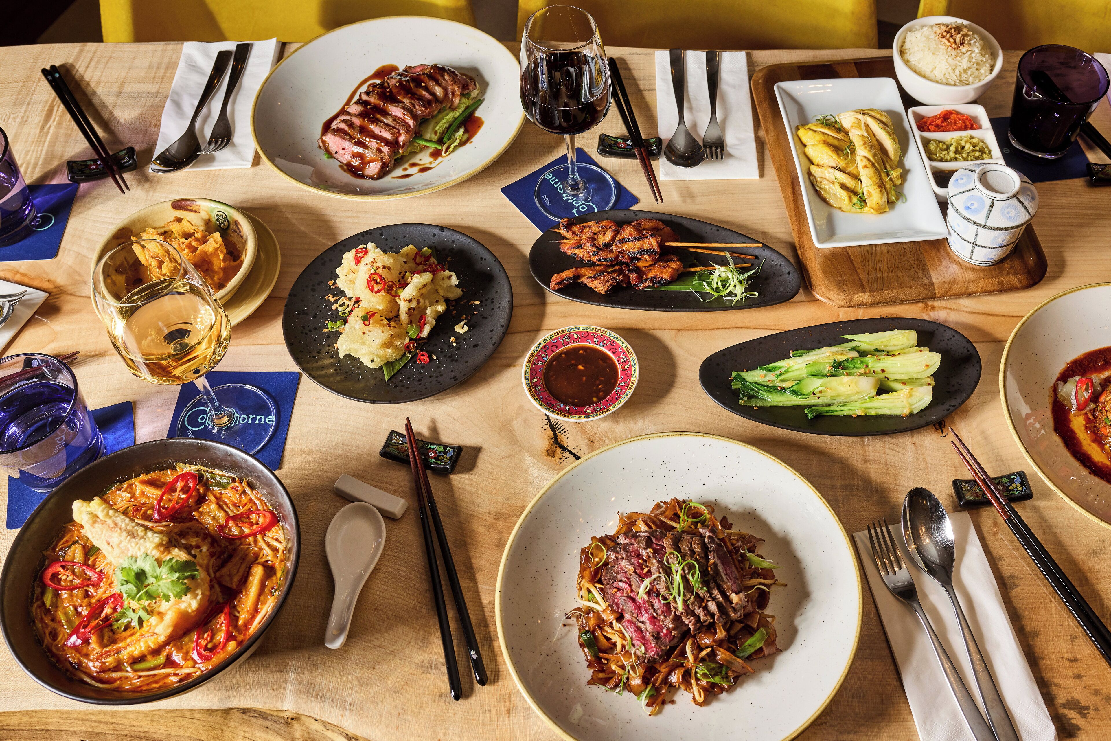 A table set with various dishes, including a steak, vegetables, and a bowl of rice.