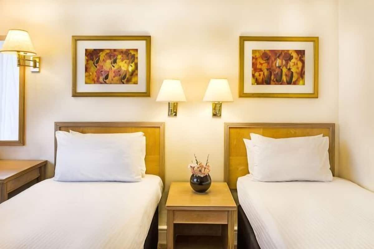Une chambre d’hôtel avec deux lits, des lampes de chevet et deux œuvres d’art encadrées accrochées au mur.