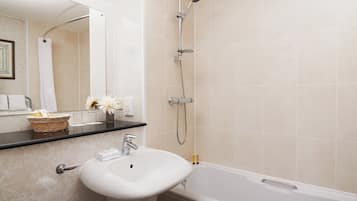 Ein Badezimmer mit einem weißen Waschbecken, einer Badewanne und einer Dusche. Über dem Waschbecken befindet sich ein Spiegel, und eine Handtuchstange mit Handtüchern.