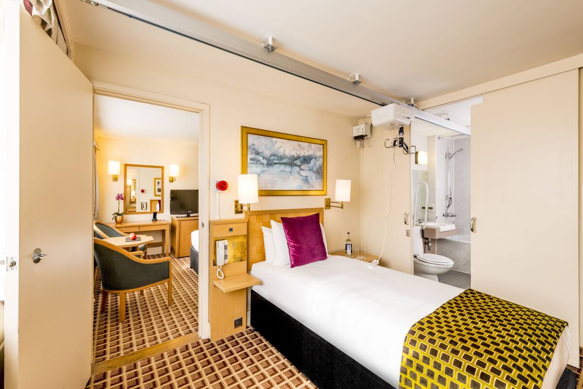 Ein Hotelzimmer mit Bett, Schreibtisch, Stuhl, Bad und einem Bild an der Wand.