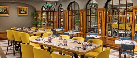 Un espace repas avec des chaises jaunes, des tables en bois et un lustre.