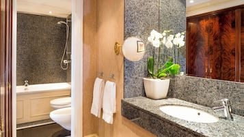 A bathroom with a granite countertop sink, a mirror, a shower, and a potted orchid.