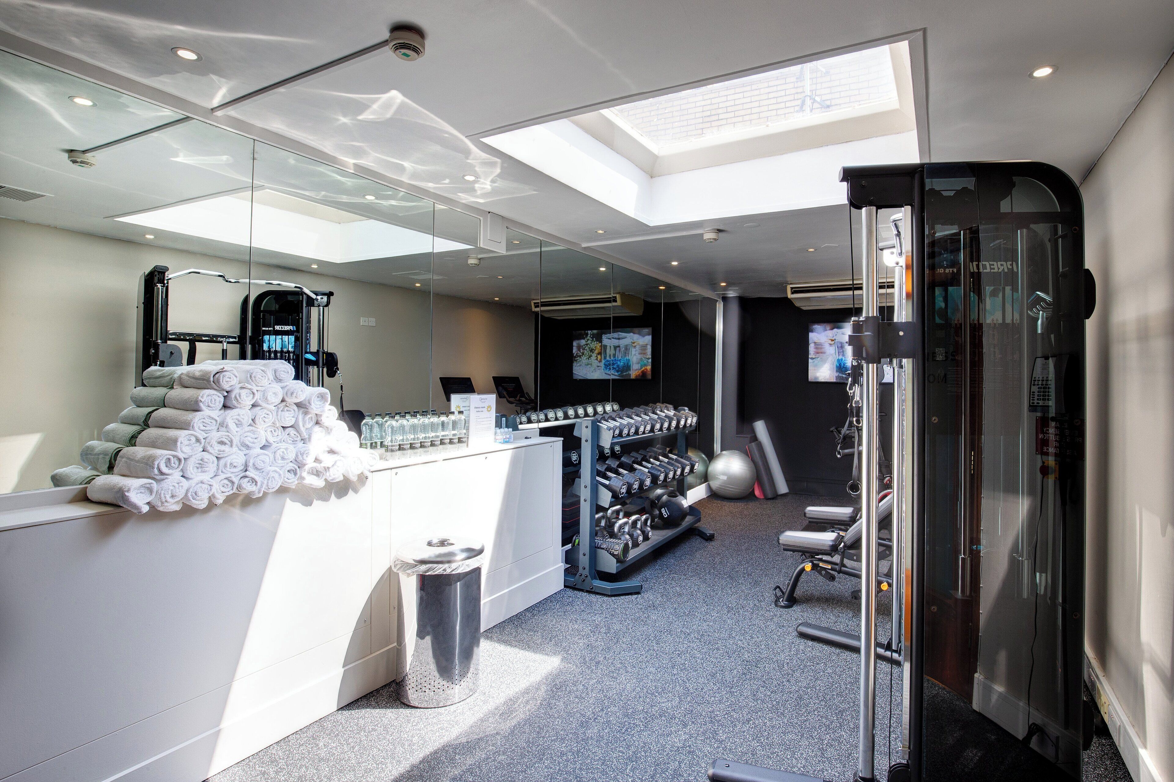 A modern gym with a skylight, weight racks, and a TV screen.
