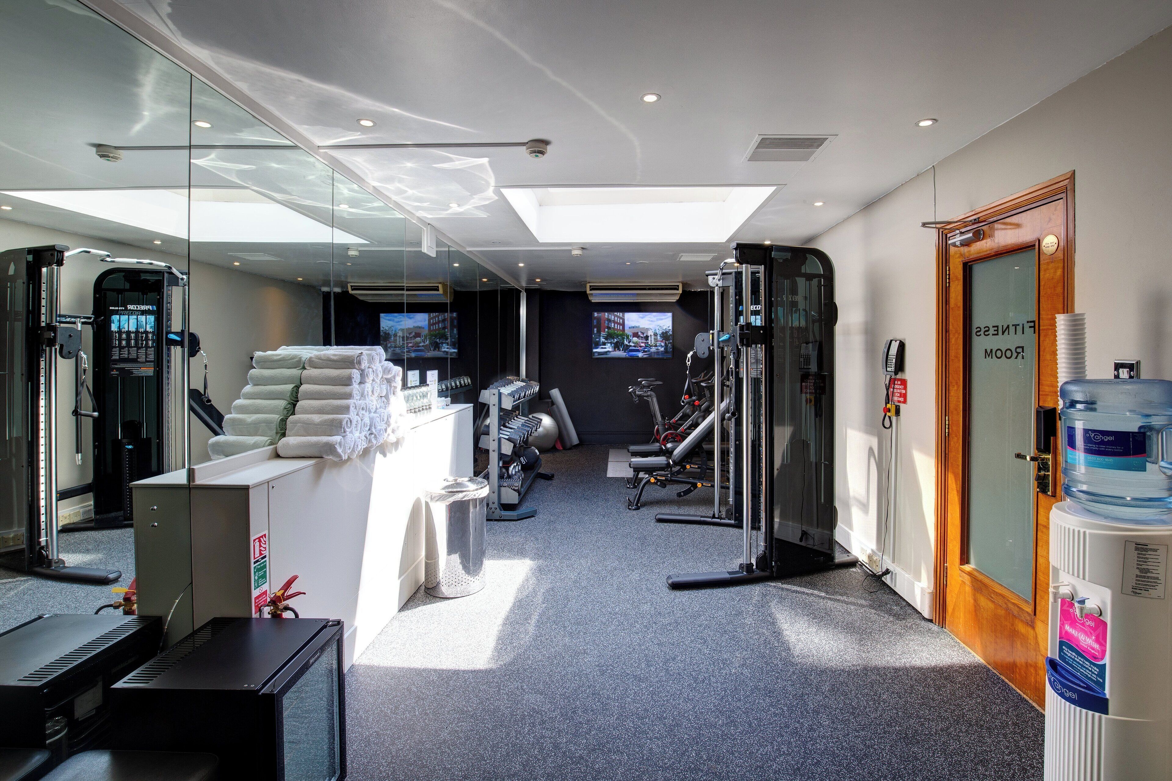 A modern fitness center with exercise equipment, a reception area, and a large water dispenser.