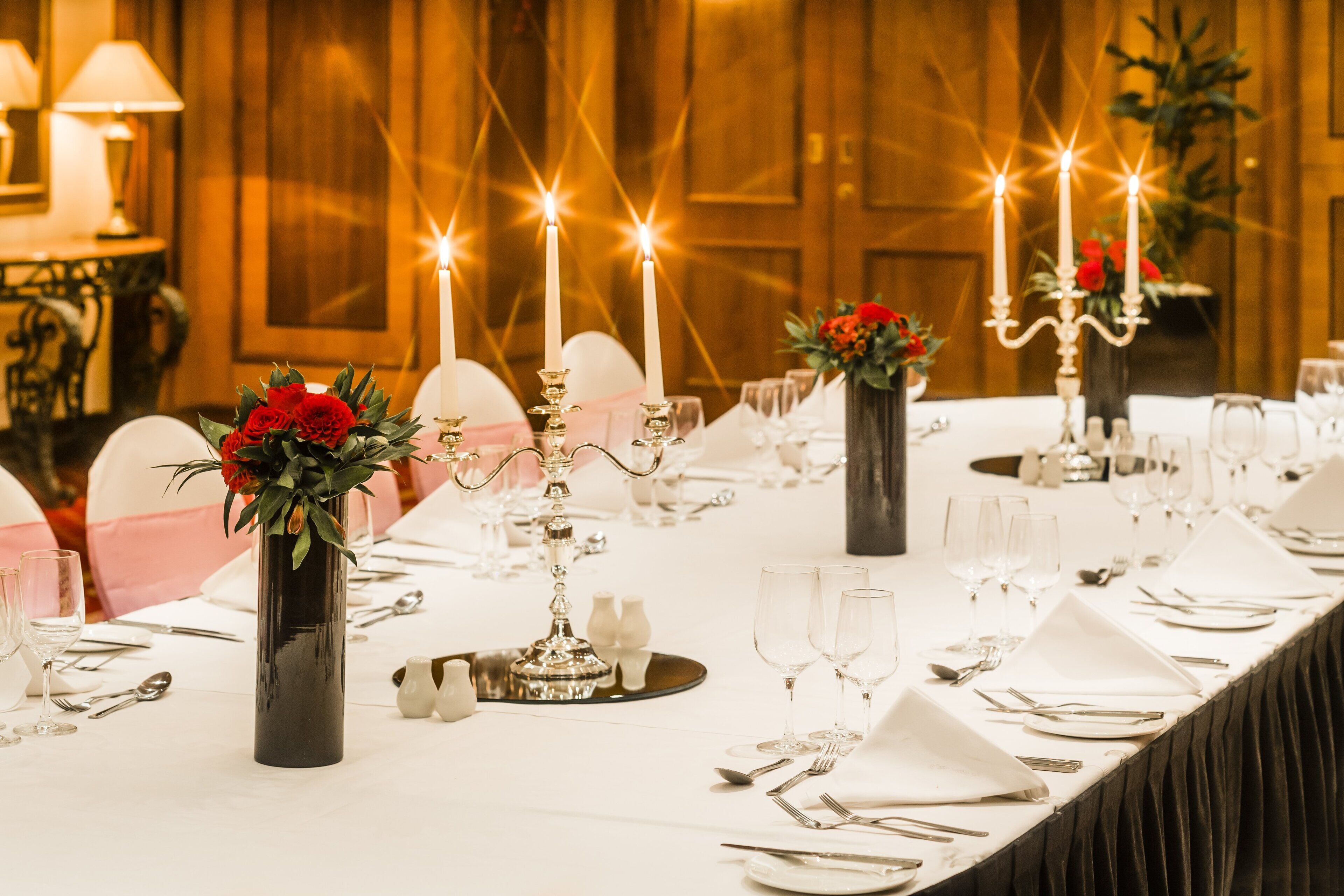 A long dining table set for a formal event with candles, glassware, and floral centerpieces.
