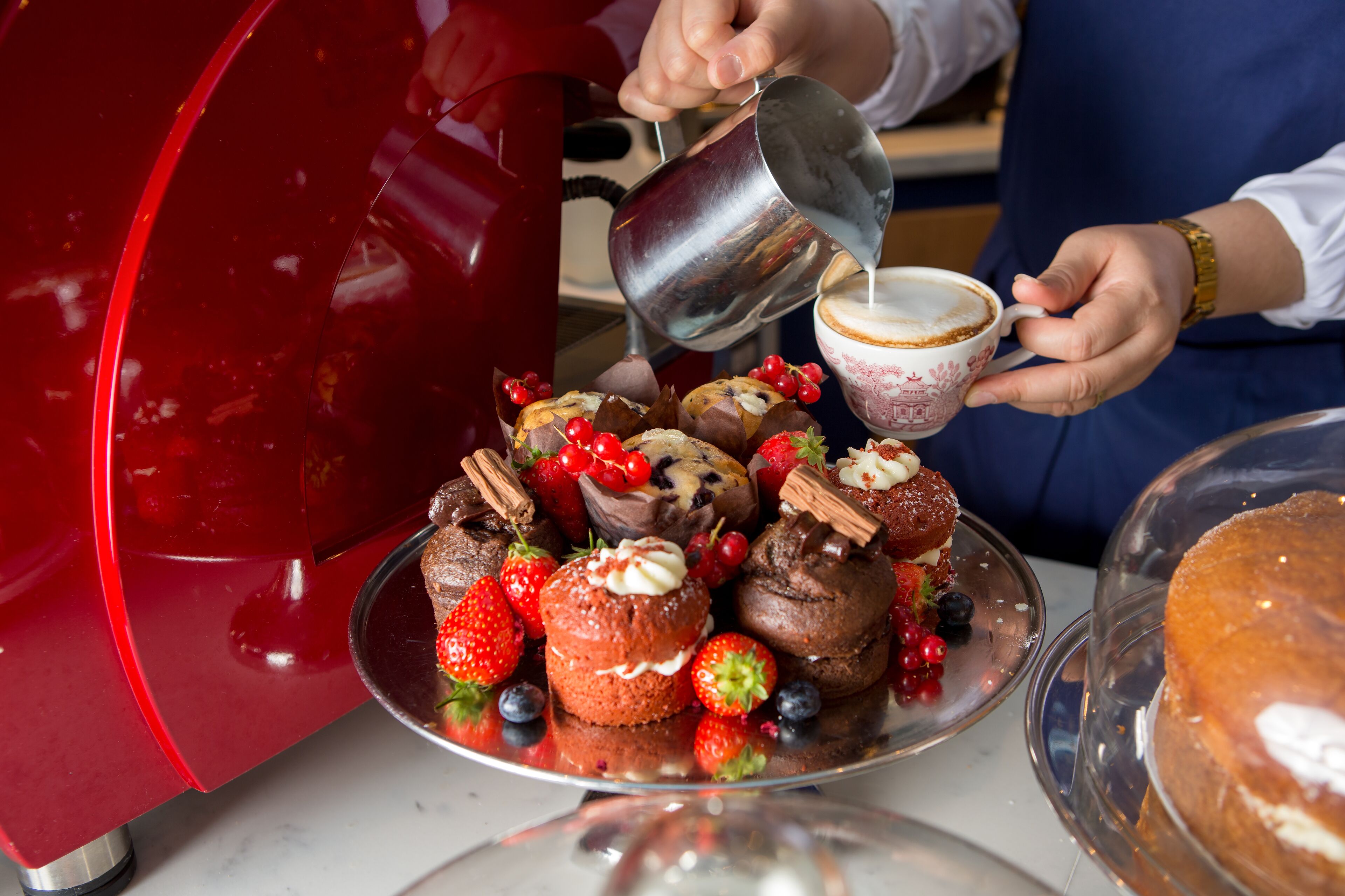 A person pouring milk into a cup next to a plate of pastries and berries.