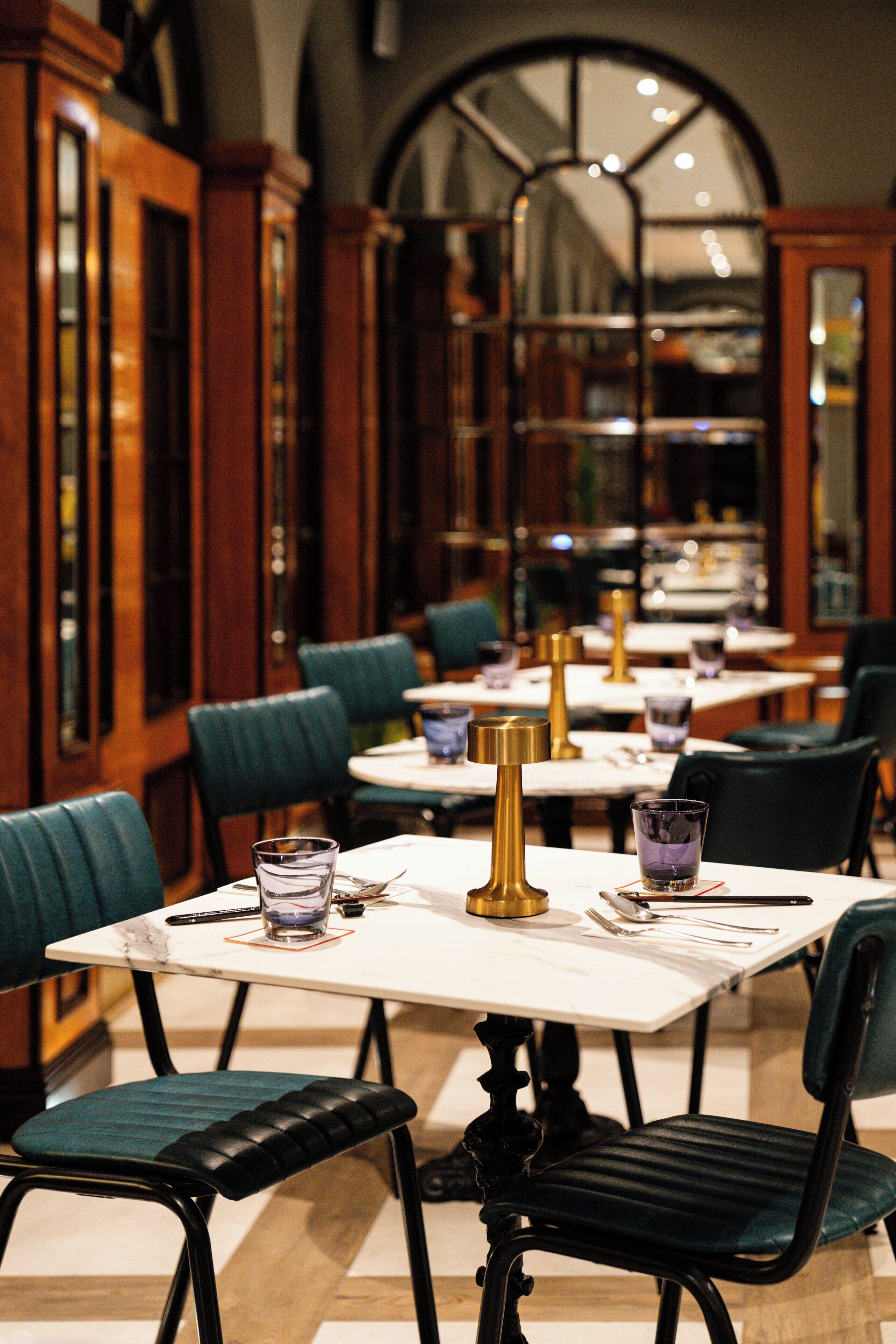 A restaurant interior with wooden cabinets, green upholstered chairs, and white tables.