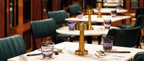 A restaurant interior with wooden cabinets, green upholstered chairs, and white tables.