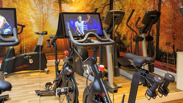 Un gimnasio con bicicletas estáticas, una cinta de correr y un espejo que refleja el equipo.