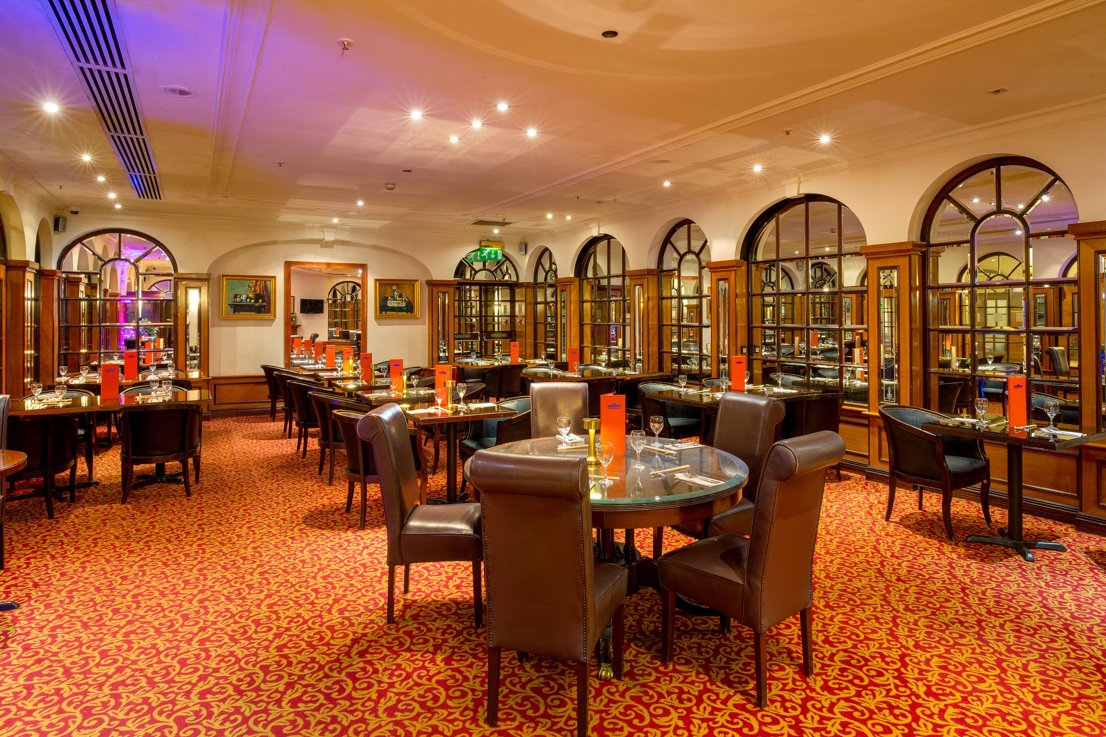 A dining area with round tables, leather chairs, and a red patterned carpet.