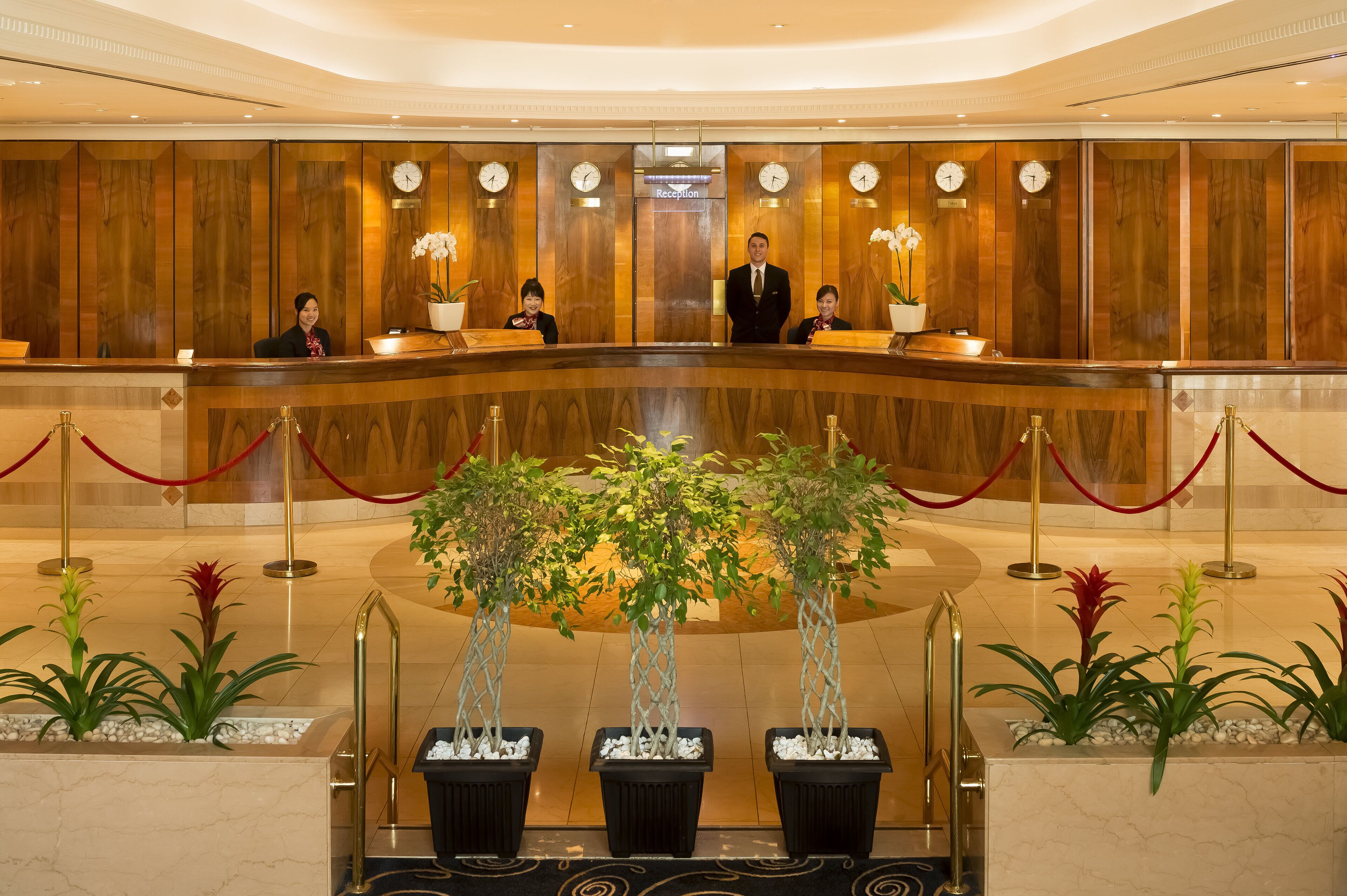 Un espace d’accueil d’hôtel avec un comptoir de réception en bois, des réceptionnistes et une horloge.