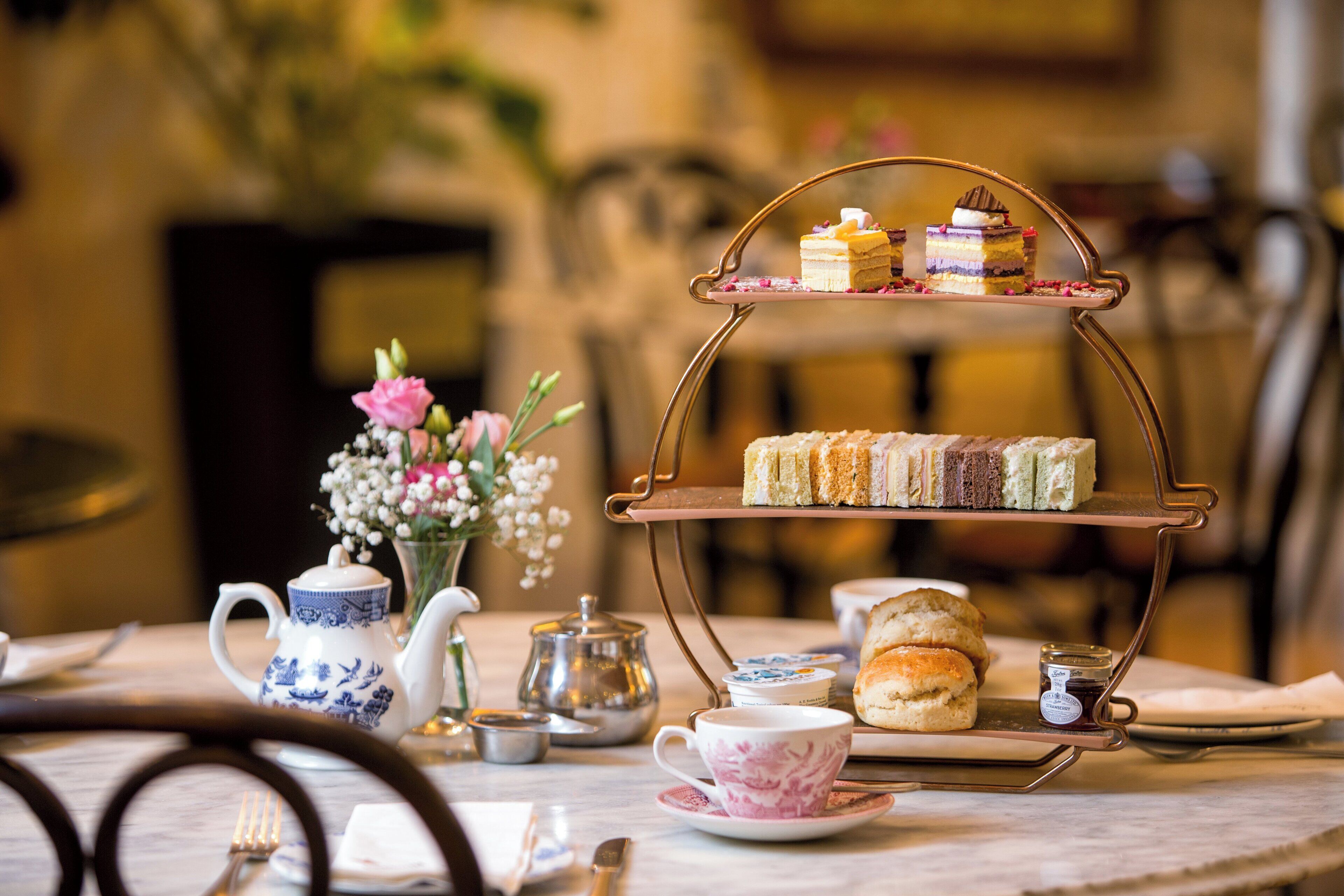 A tea service setup with a teapot, cups, and a tiered stand holding sandwiches and scones.