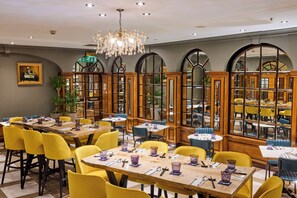 Un ristorante con tavoli in legno e sedie gialle, un lampadario e ampie finestre ad arco.