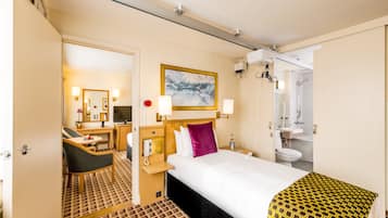 Habitación de hotel con cama, escritorio, silla, baño con ducha y un cuadro en la pared.