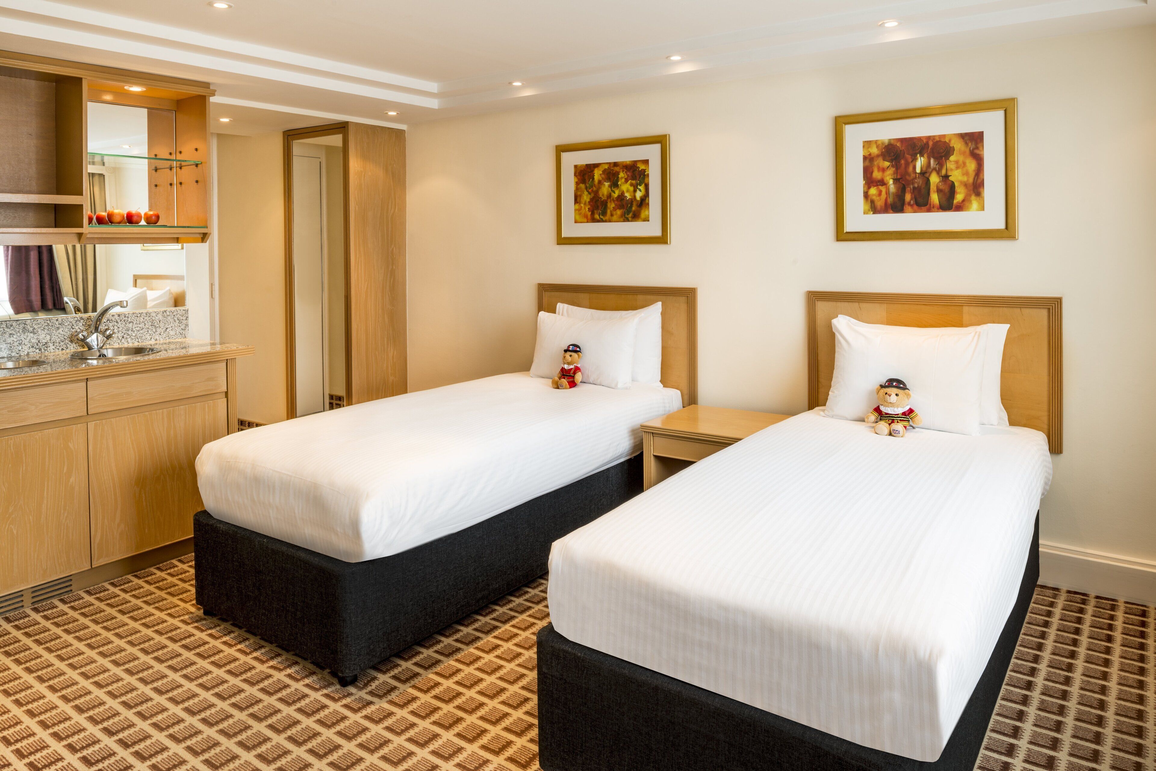 Une chambre d’hôtel avec deux lits, une petite salle de bain, une kitchenette et des œuvres d’art accrochées aux murs.