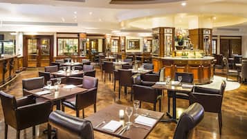Un restaurante amplio con varias mesas y sillas, una zona de bar y vistas al exterior a través de amplios ventanales.