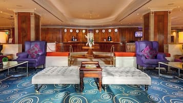A lobby with a reception desk, two purple armchairs, a tufted ottoman, and a patterned carpet.