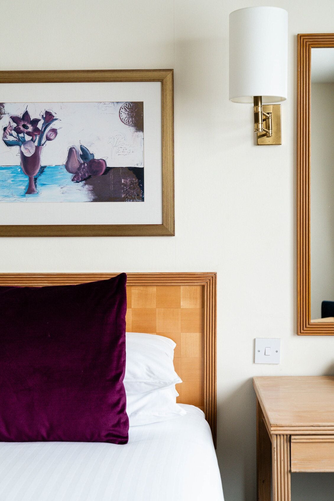 A hotel room with a bed, a framed artwork of flowers, a bedside lamp, and a nightstand.