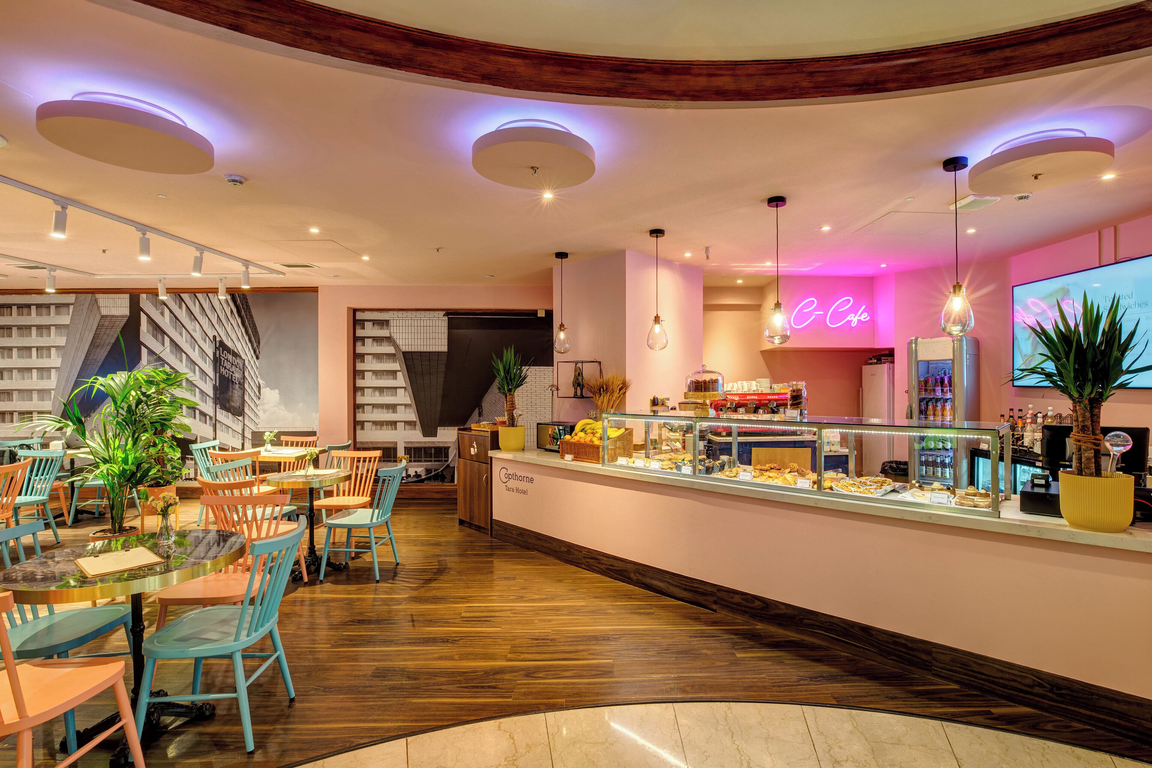 Un café moderne avec un comptoir central, un espace salon et un panneau lumineux au néon.