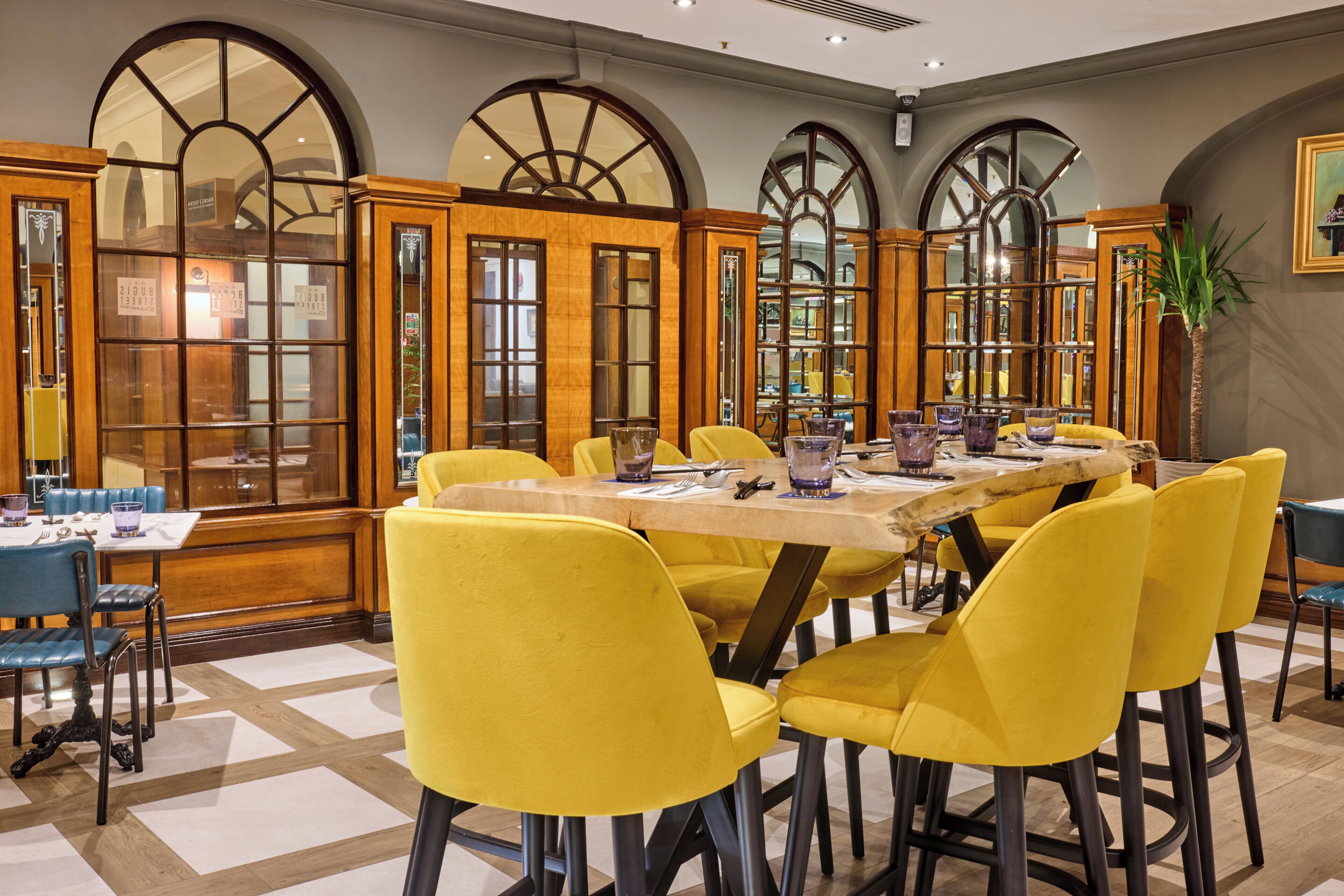 Un comedor con mesa de madera, sillas amarillas y ventanas arqueadas amplias.