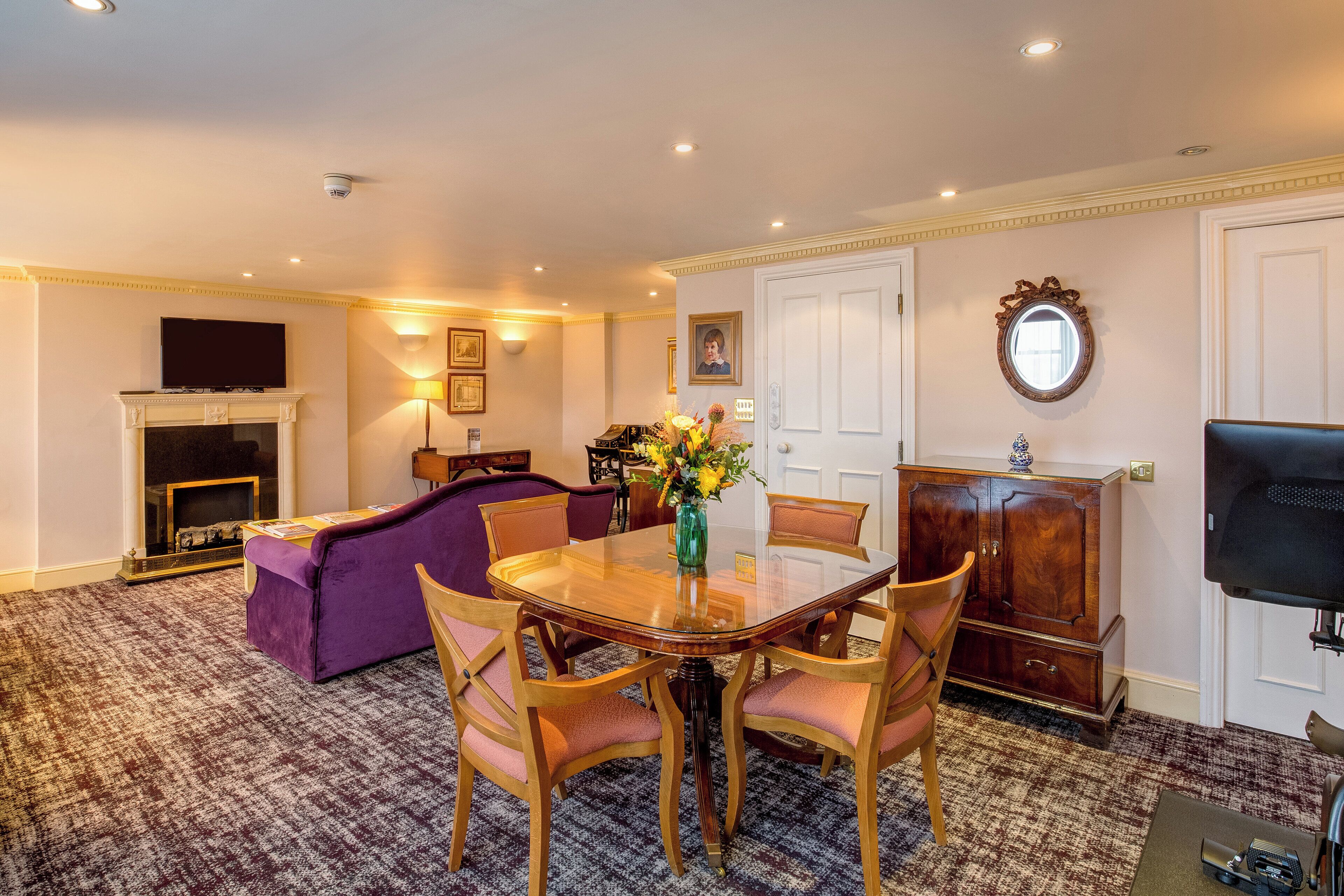 A dining area with a wooden table and chairs, a fireplace, a sofa, and a television.