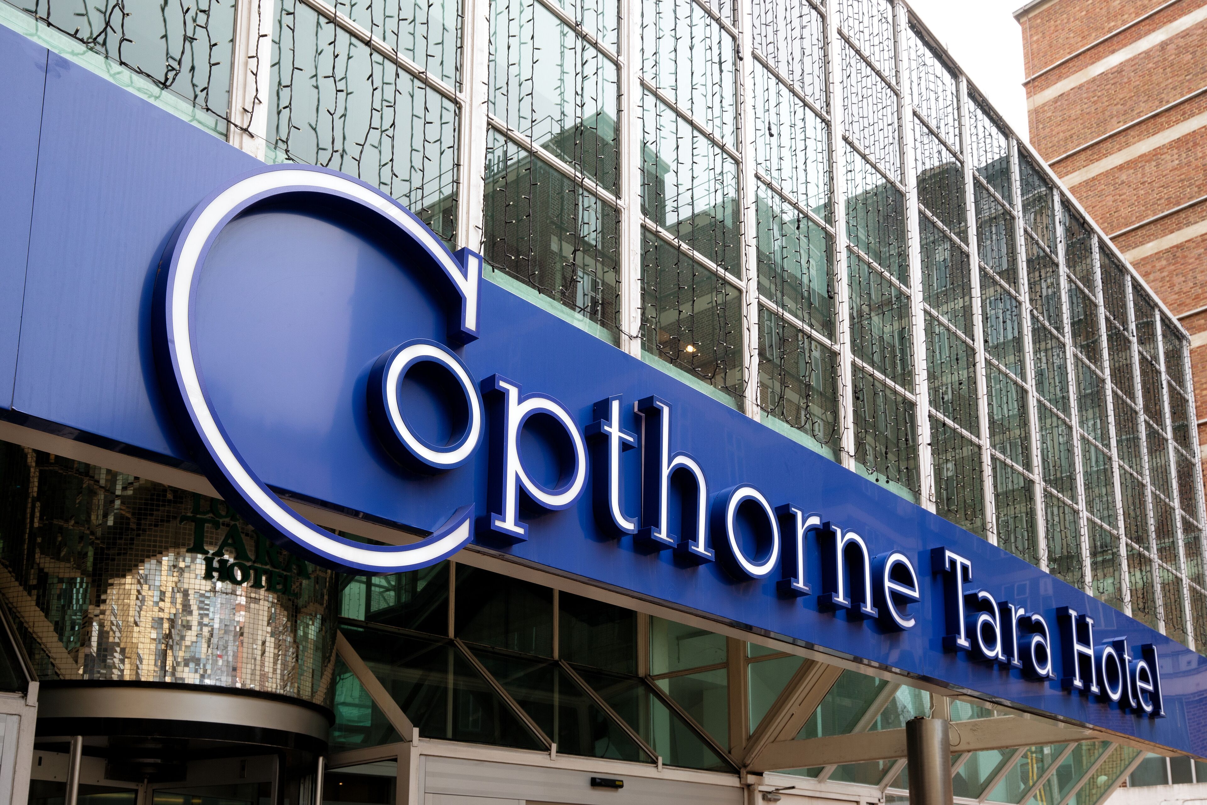 The exterior of the Opthorne Tara Hotel with a modern glass facade and a prominent blue sign.