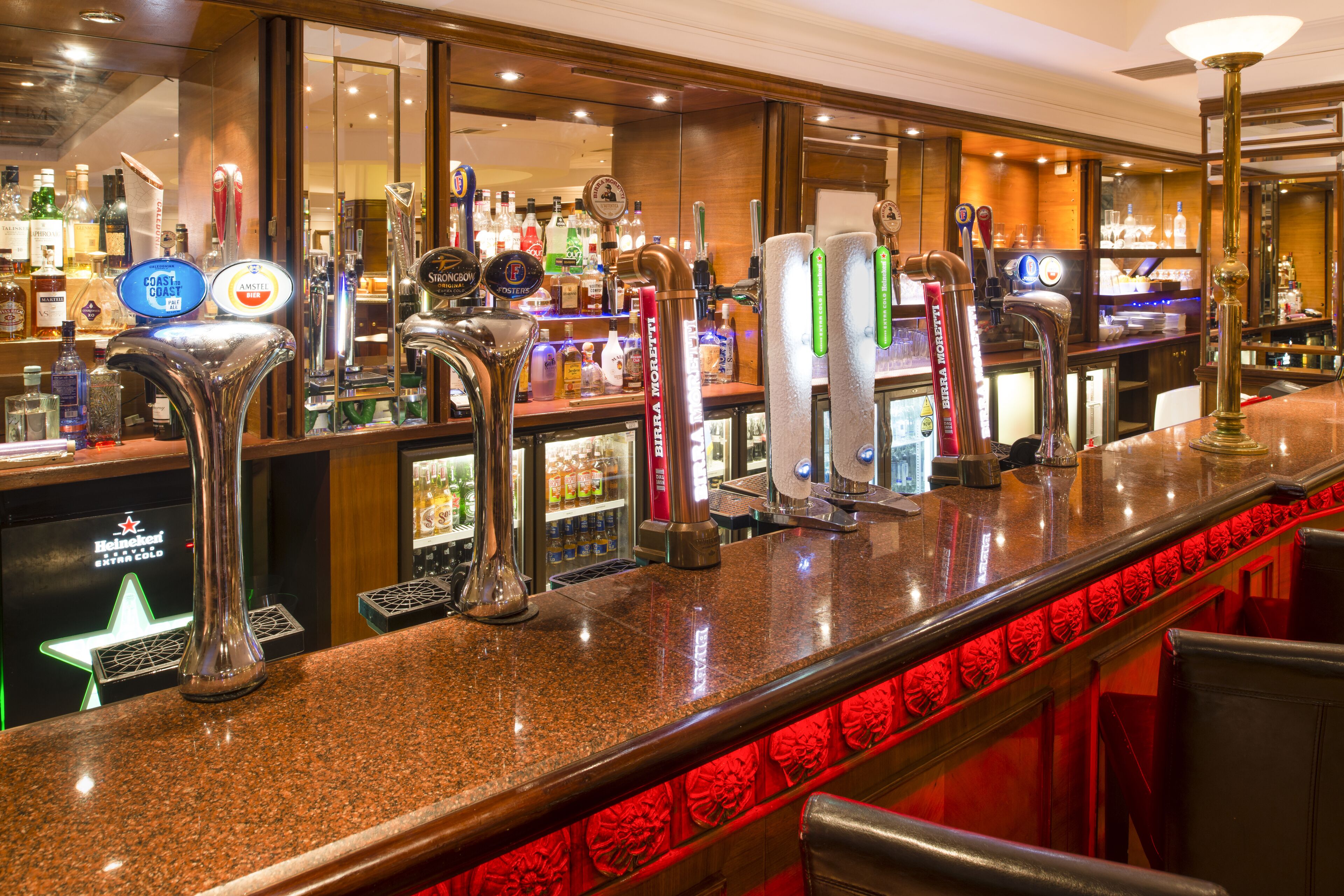 A bar area with multiple taps, a refrigerated display, and a variety of bottles.