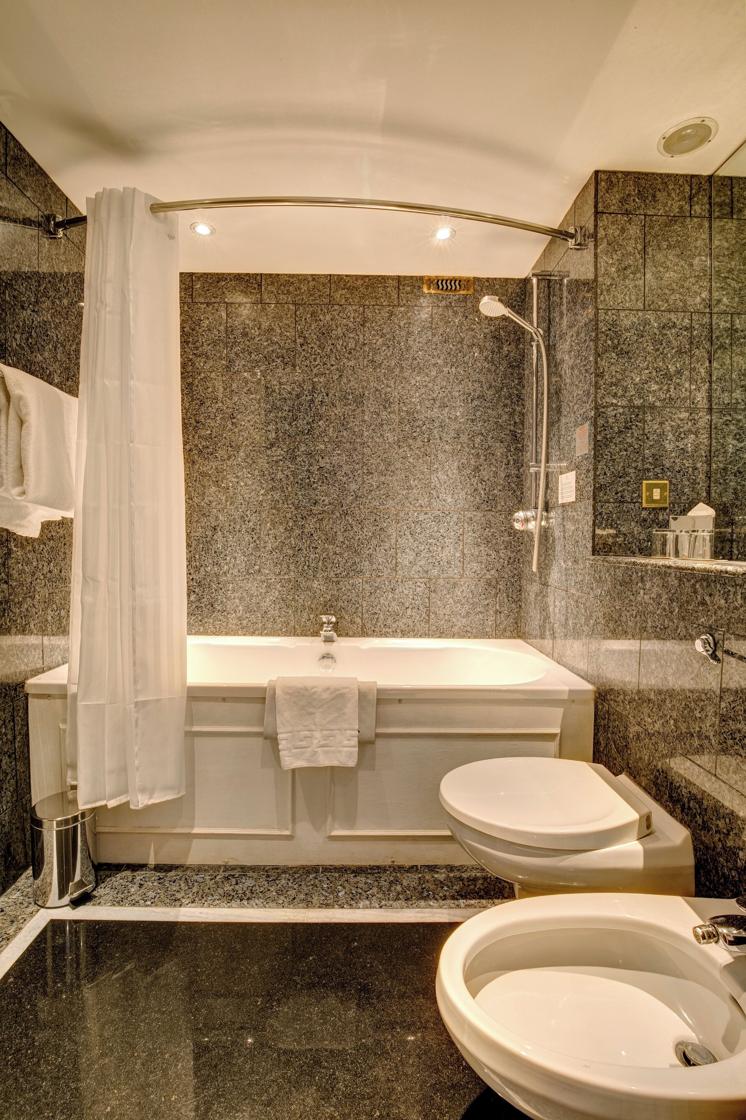 A modern bathroom with a freestanding bathtub, two toilets, and a large mirror.