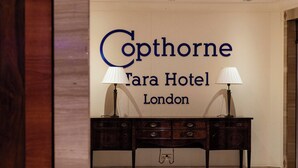 A reception area with a sign for Copthorne Tara Hotel London, a wooden desk with two lamps, and a tiled floor. - Copthorne Tara Hotel London Kensington (London)