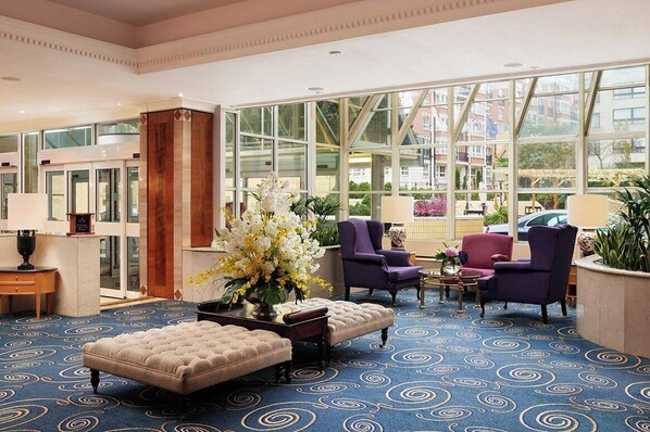 Un vestíbulo de hotel con un ventanal grande, una alfombra de diseño azulado y sillones morados.