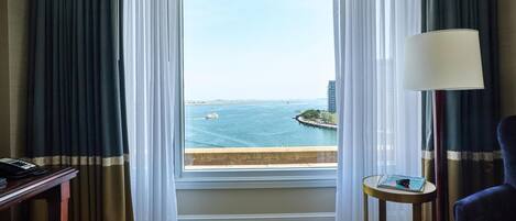 A hotel room with a large window, a desk, a chair, and a lamp.